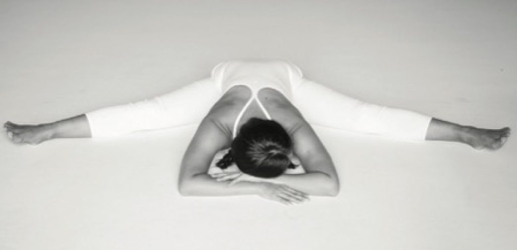 Woman sitting on the ground in Yin yoga dragonfly pose.