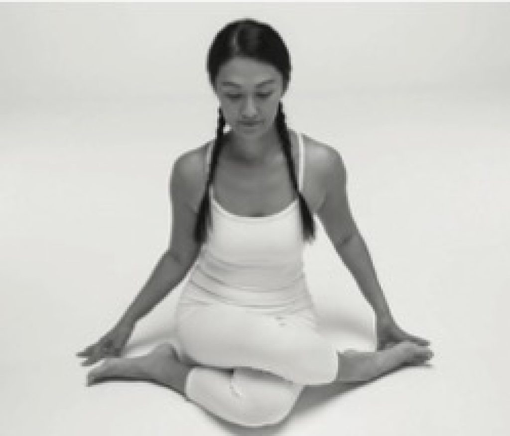 Woman sitting upright with her knees stacked on top of each other doing Yin yoga shoelace pose.