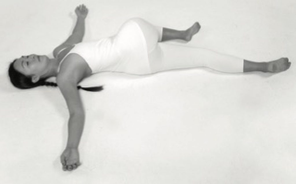 Woman lying on her back with one leg stretching over the side of her body doing Twist Yin yoga pose.