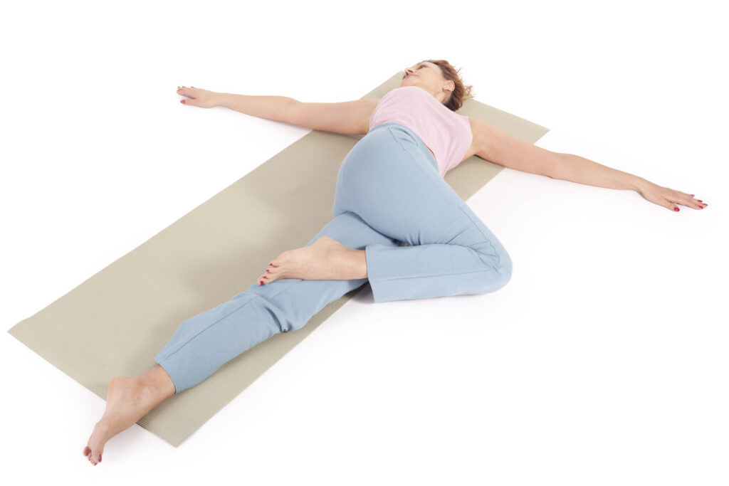 Female practicing yoga in reclined twist pose.