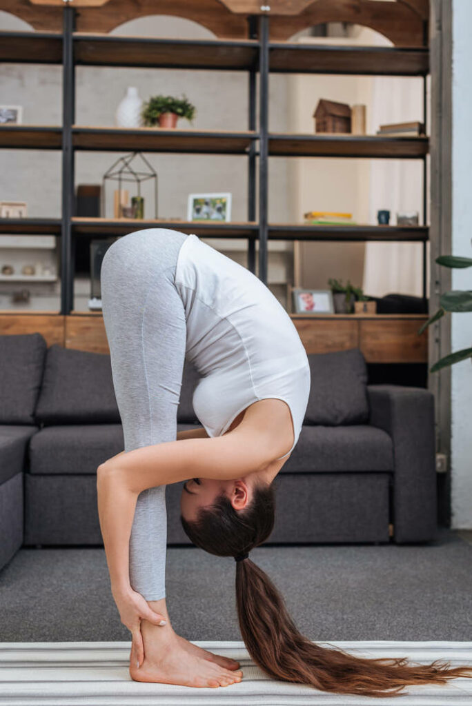 Female yogi in standing forward fold while practicing yoga at home