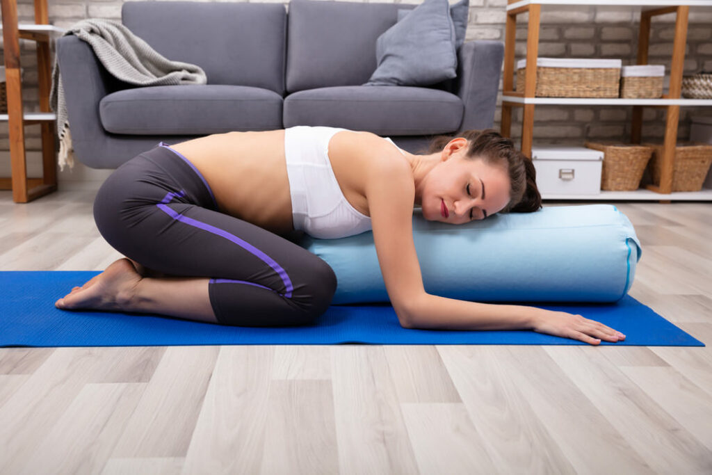 Woman practicing restorative yoga using a prop in supported child's pose.