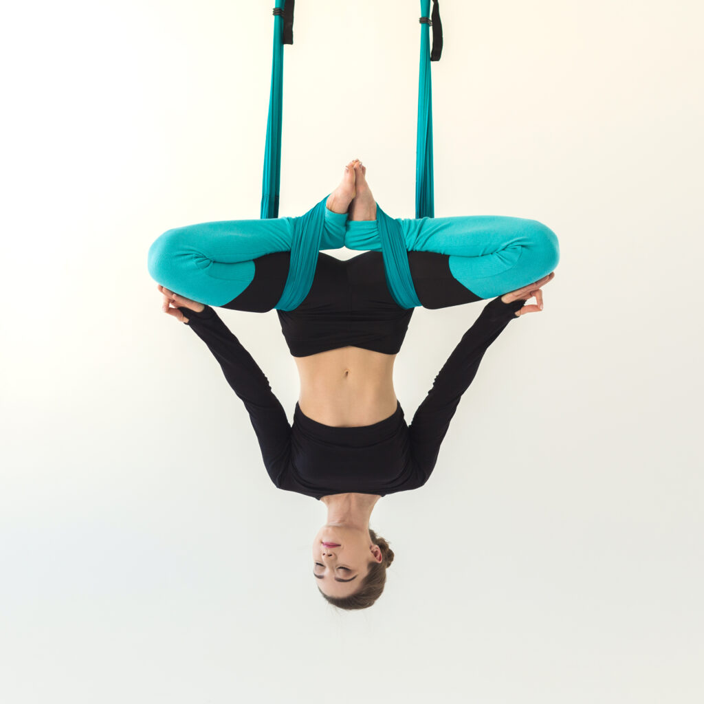 Concentrated focused woman performing inverted butterfly pose during aerial  yoga group workout in fitness studio, hanging upside down in hammock with  arms twisted.. Stock Photo | Adobe Stock