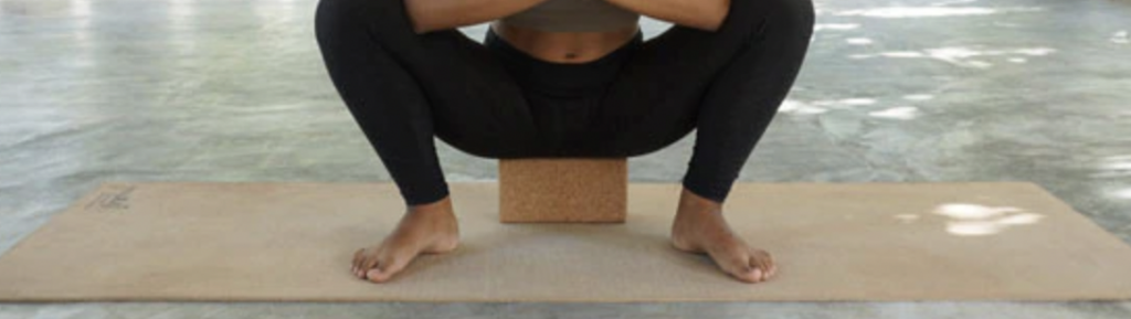 Woman performing malasana modification by sitting on a yoga block.