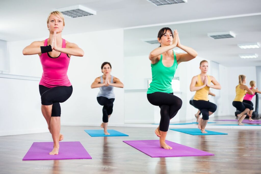 Group of female yogis practicing Bikram yoga doing Eagle pose.