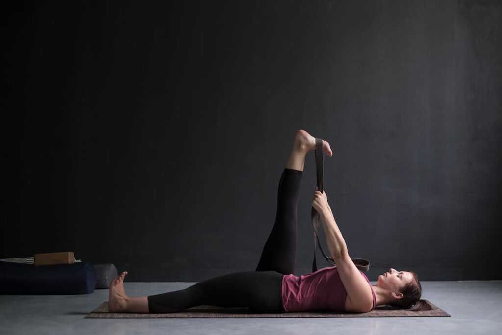 Female yogi practicing Iyengar yoga using a strap to stretch her extended leg.