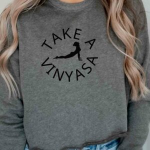 Female yogi wearing gray funny yoga ladies' sweatshirt that says take a vinyasa.