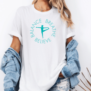 Female yogi with long hair wearing a white yoga t-shirt with a graphic of a yogi doing a yoga pose and says Balance Breathe Believe.