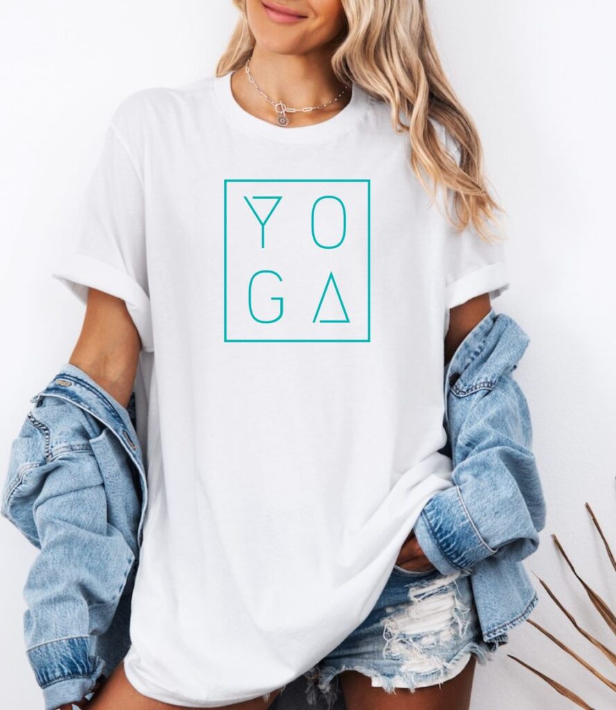 Female yogi with long hair wearing a casual white yoga graphic print t-shirt with the word yoga printed in a modern minimalist font with a box outline.