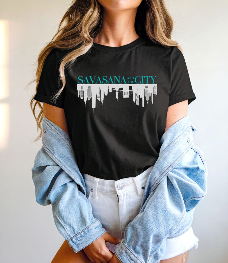 Female yogi with long hair wearing a black yoga t-shirt with a savasana and the city graphic design.