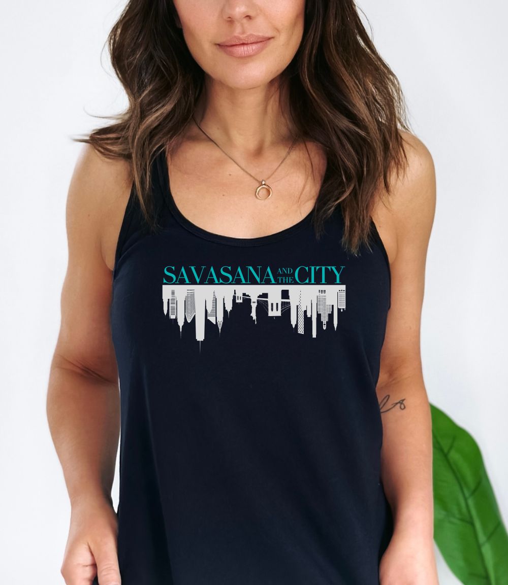 Female yogi with long brown hair wearing a black racerback yoga tank top with a savasana and the city graphic print.